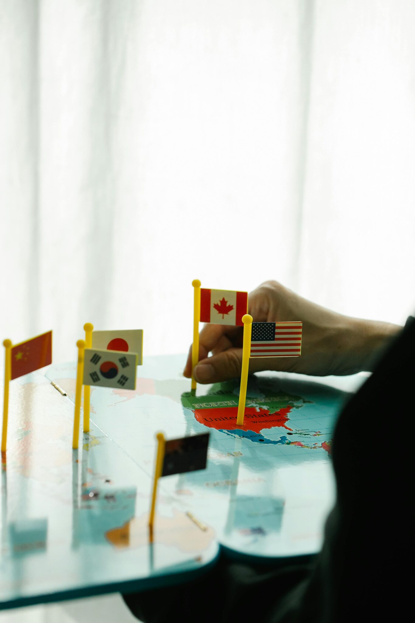 A person places miniature flags on a colorful world map indoors, showcasing global diversity.